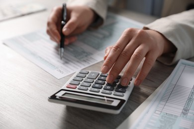 Photo of Payroll. Woman using calculator while working with tax return forms at wooden table, selective focus