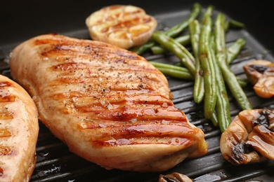 Photo of Tasty grilled chicken fillets and vegetables on frying pan, closeup