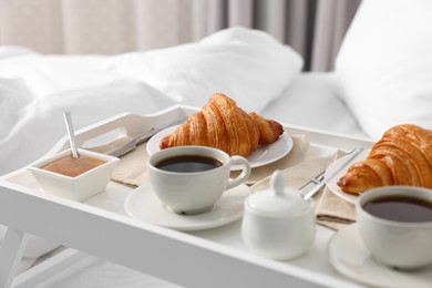 Photo of Tasty breakfast served in bed. Fresh croissants, coffee and honey on tray, closeup