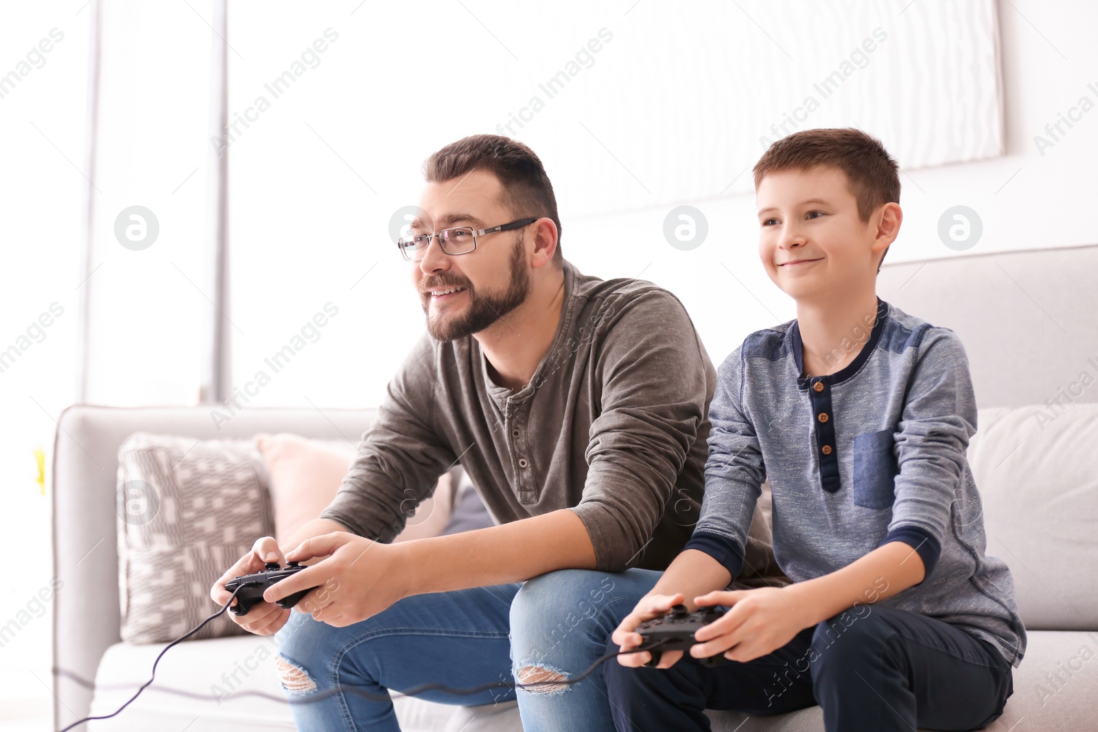 Photo of Little boy and his dad playing video game together at home
