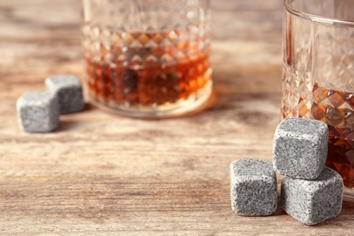 Whiskey stones and glass with liquor on wooden table, closeup