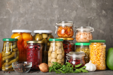 Glass jars with different pickled vegetables on grey table