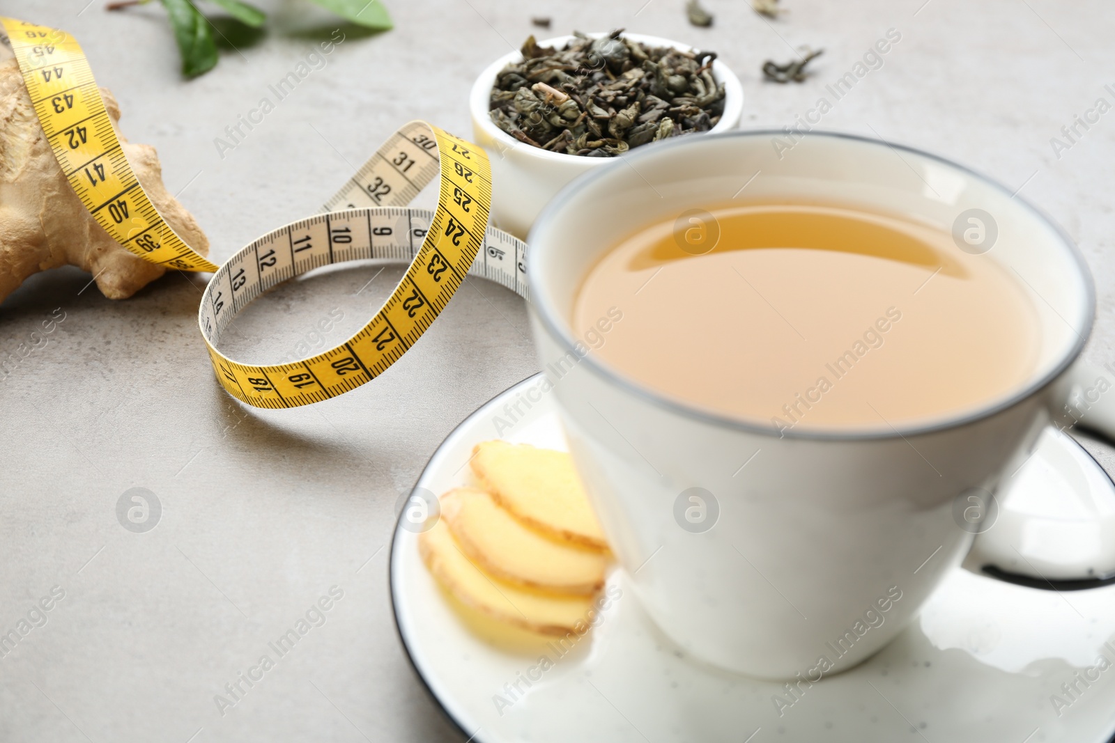 Photo of Cup of herbal diet tea and measuring tape on light table, closeup