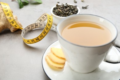 Photo of Cup of herbal diet tea and measuring tape on light table, closeup