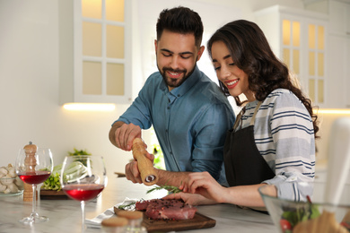 Photo of Lovely young couple cooking meat together in kitchen