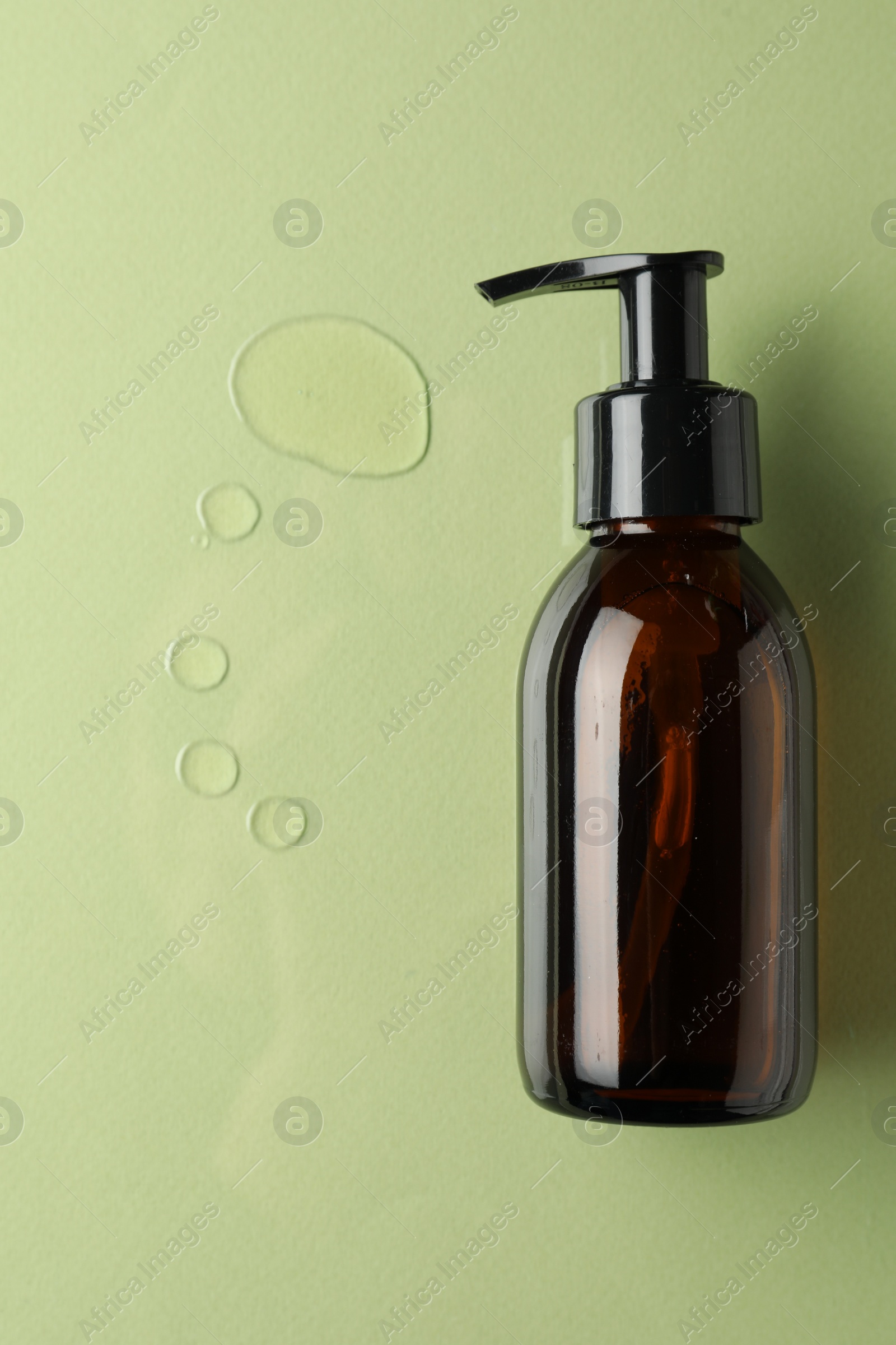 Photo of Bottle and drops of hydrophilic oil on light green background, flat lay