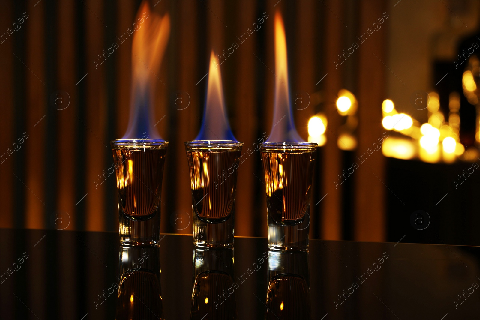 Photo of Flaming alcohol drink in shot glasses on mirror surface against blurred background