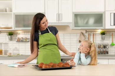 Photo of Daughter and mother with tray of oven baked buns at table in kitchen