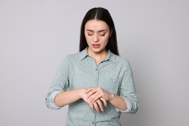 Photo of Young woman suffering from pain in hands on light grey background. Arthritis symptoms