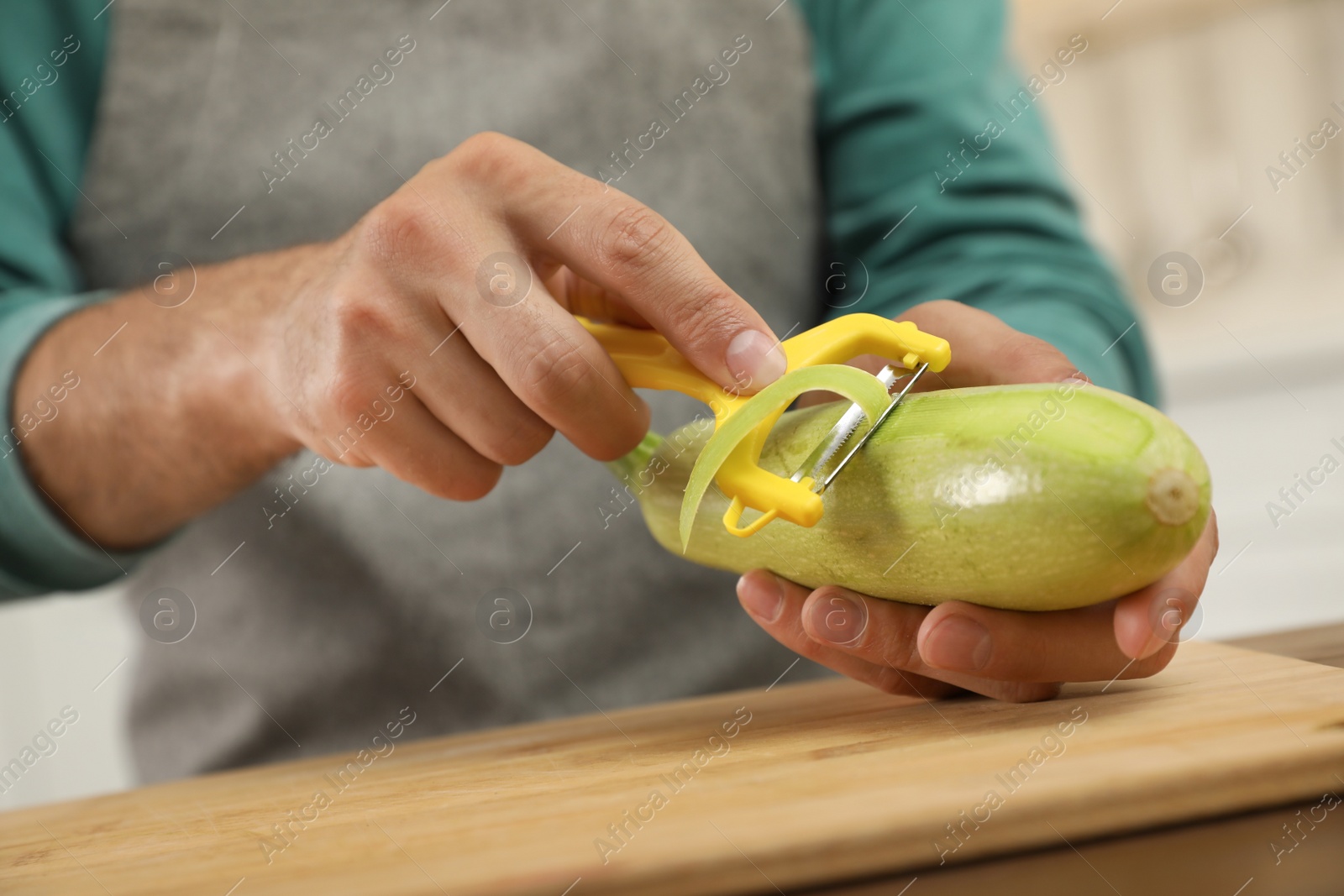 Photo of Man peeling zucchini at kitchen table, closeup. Preparing vegetable