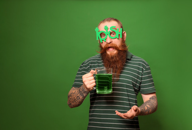 Bearded man in party glasses with green beer on color background, space for text. St. Patrick's Day celebration