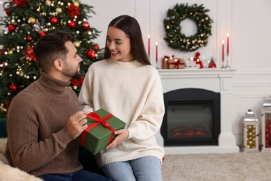 Photo of Beautiful young woman giving Christmas gift to her boyfriend at home