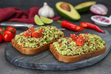 Slices of bread with tasty guacamole and ingredients on grey table, closeup