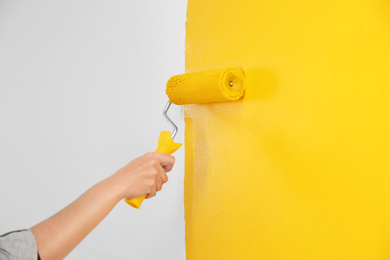 Photo of Woman painting white wall with yellow dye, closeup. Interior renovation