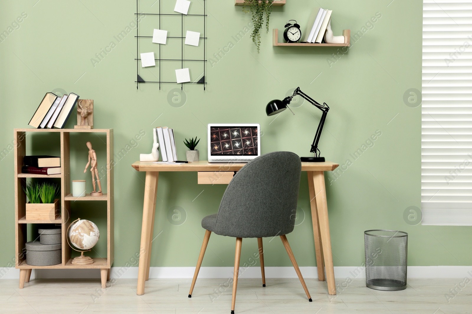 Photo of Workplace with modern laptop on wooden desk, bookcase and cosy chair at home