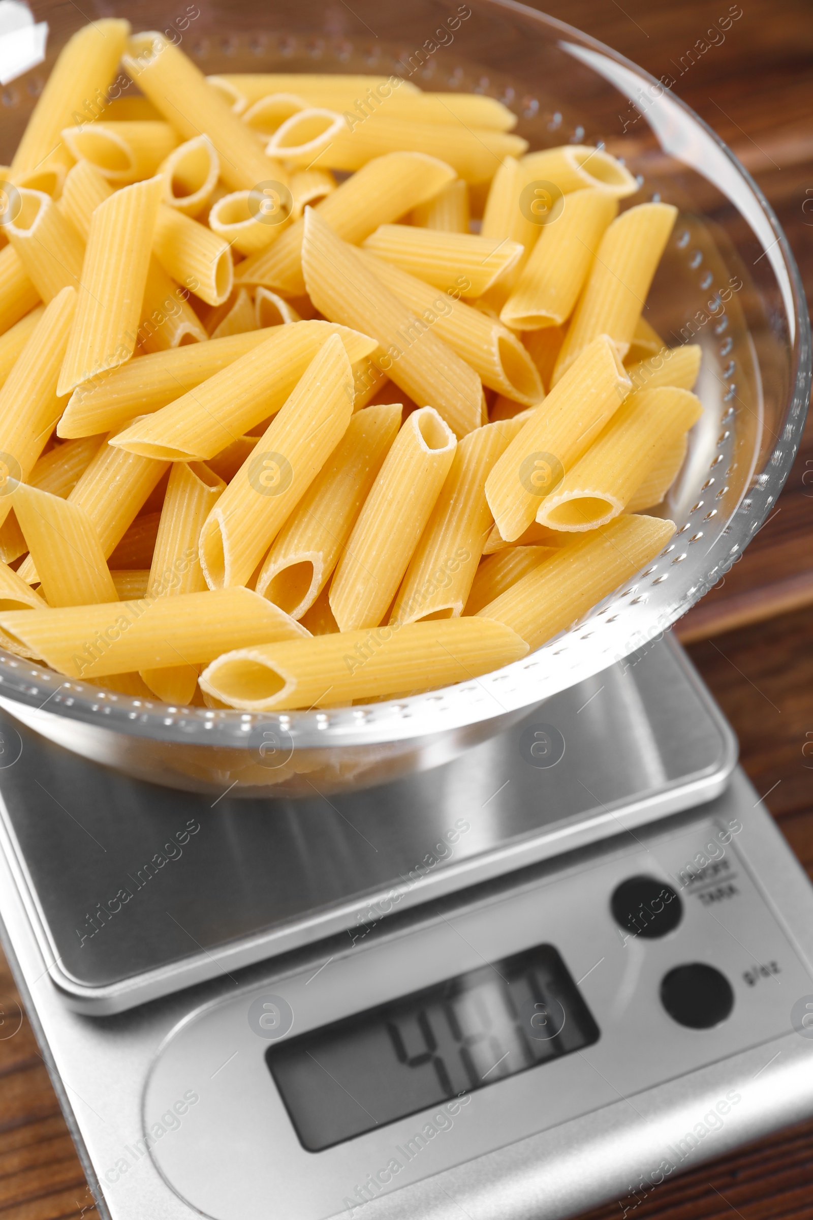 Photo of Kitchen scale with bowl of pasta on wooden table, closeup