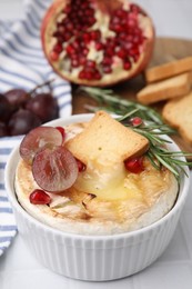 Photo of Tasty baked camembert with crouton, grape and rosemary on white tiled table, closeup