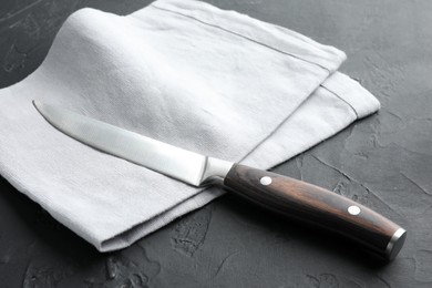 Photo of One sharp knife and napkin on dark textured table, closeup