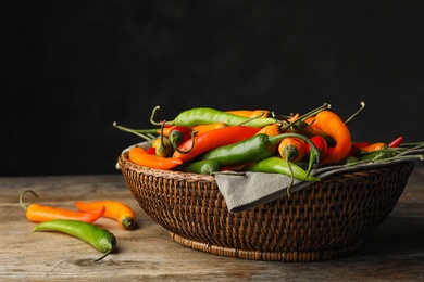 Photo of Wicker bowl with different chili peppers on wooden table. Space for text