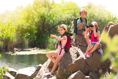Image of School holidays. Group of happy children sitting on rocks near river 