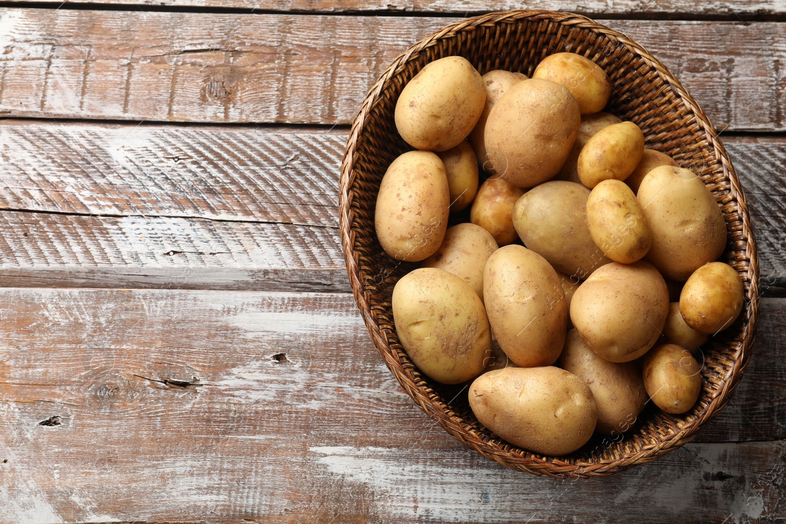 Photo of Raw fresh potatoes in wicker basket on wooden table, top view. Space for text