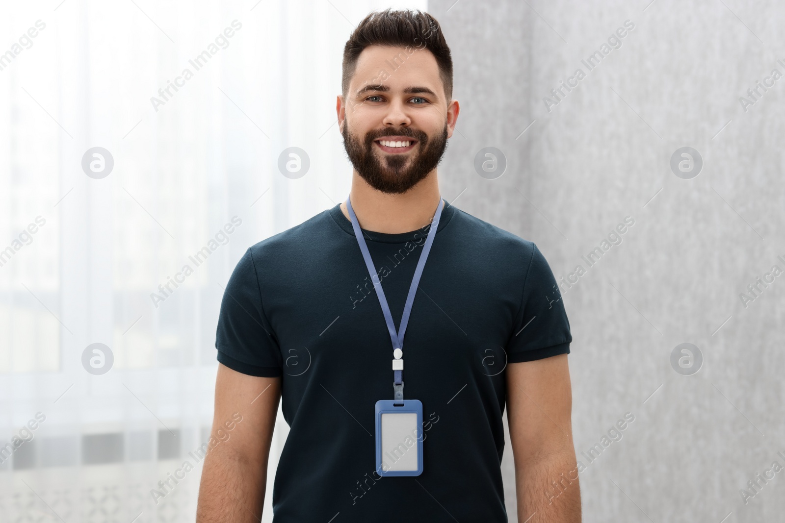 Photo of Happy young man with blank badge indoors