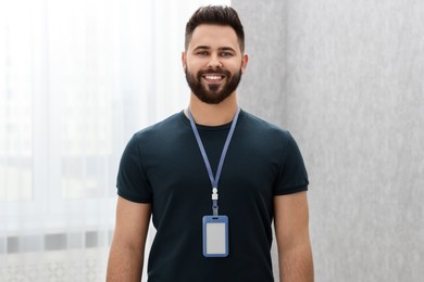 Happy young man with blank badge indoors