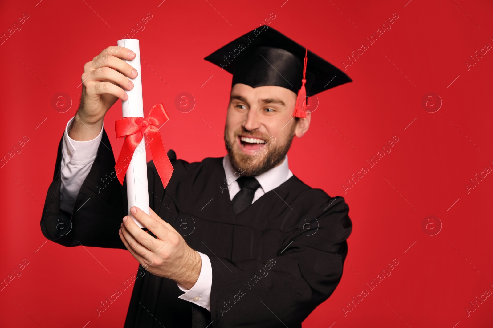 Photo of Happy student with graduation hat against red background, focus on diploma