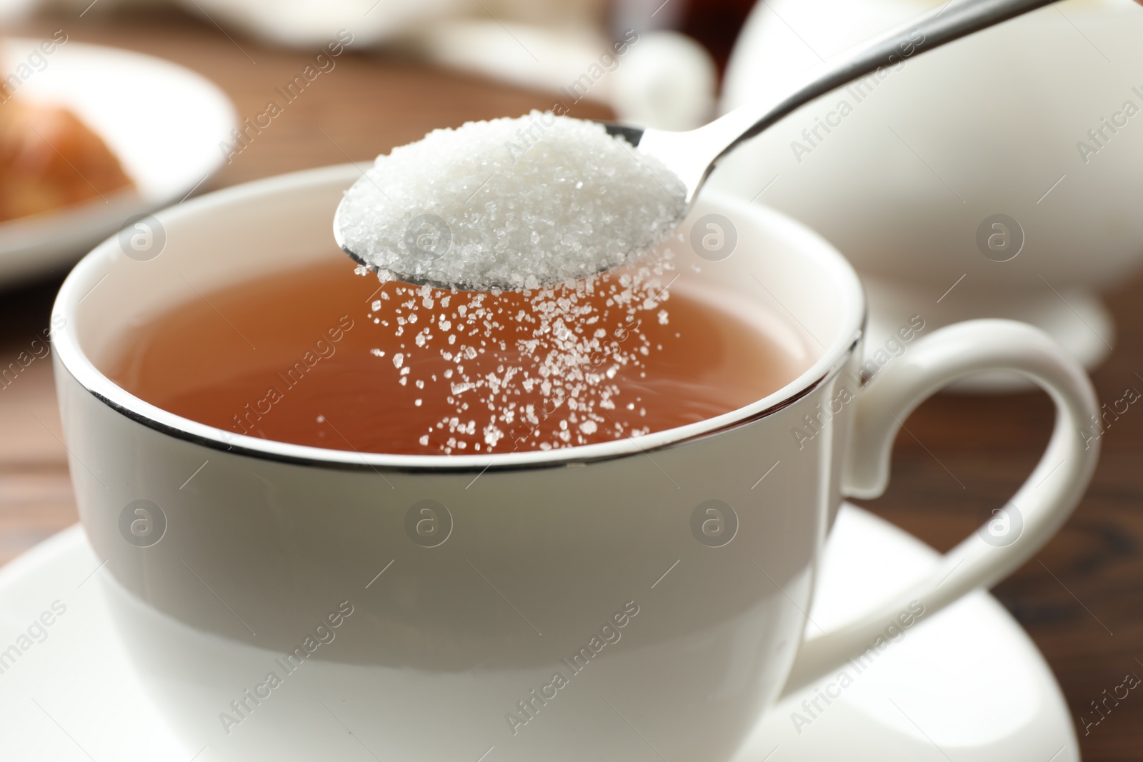 Photo of Adding sugar into cup of tea at table, closeup