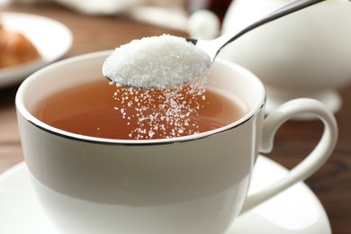 Adding sugar into cup of tea at table, closeup