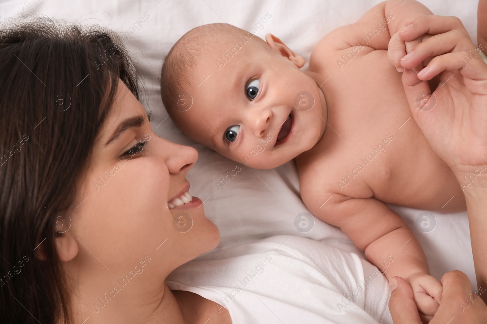 Photo of Happy young mother with her cute baby on bed, top view