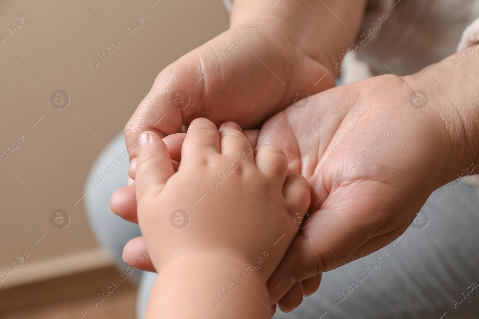 Photo of Woman holding hands with her granddaughter on beige background, closeup