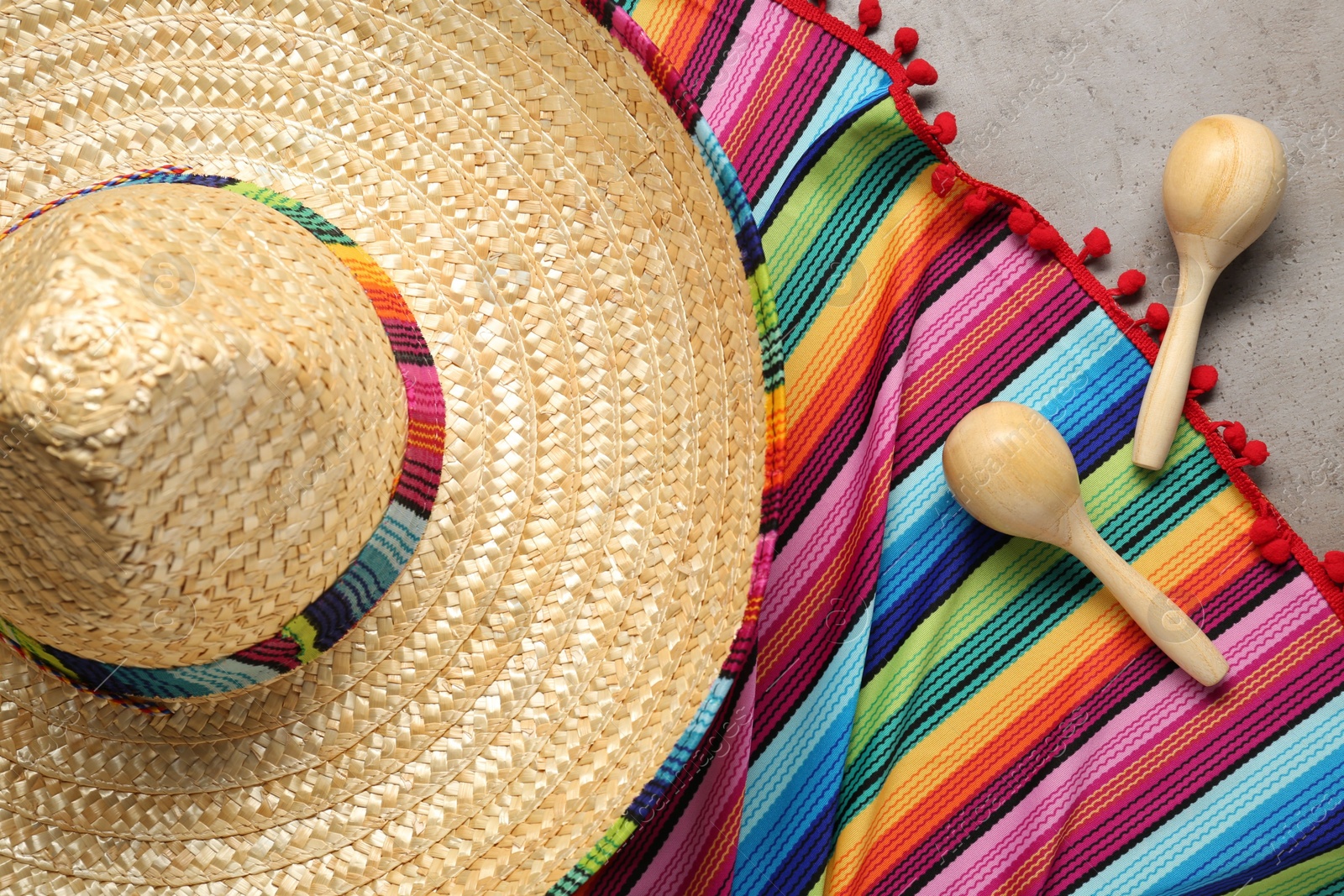 Photo of Mexican sombrero hat, maracas and colorful poncho on grey background, flat lay