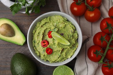 Bowl of delicious guacamole and ingredients on wooden table, flat lay