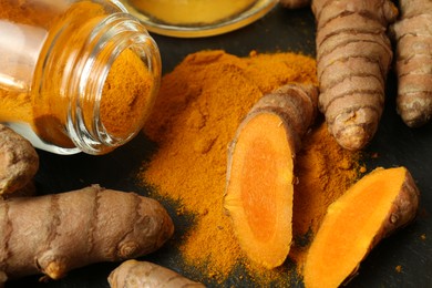 Turmeric roots and powder on black textured table, closeup