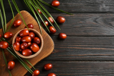 Palm oil fruits in bowl on black wooden table, flat lay. Space for text