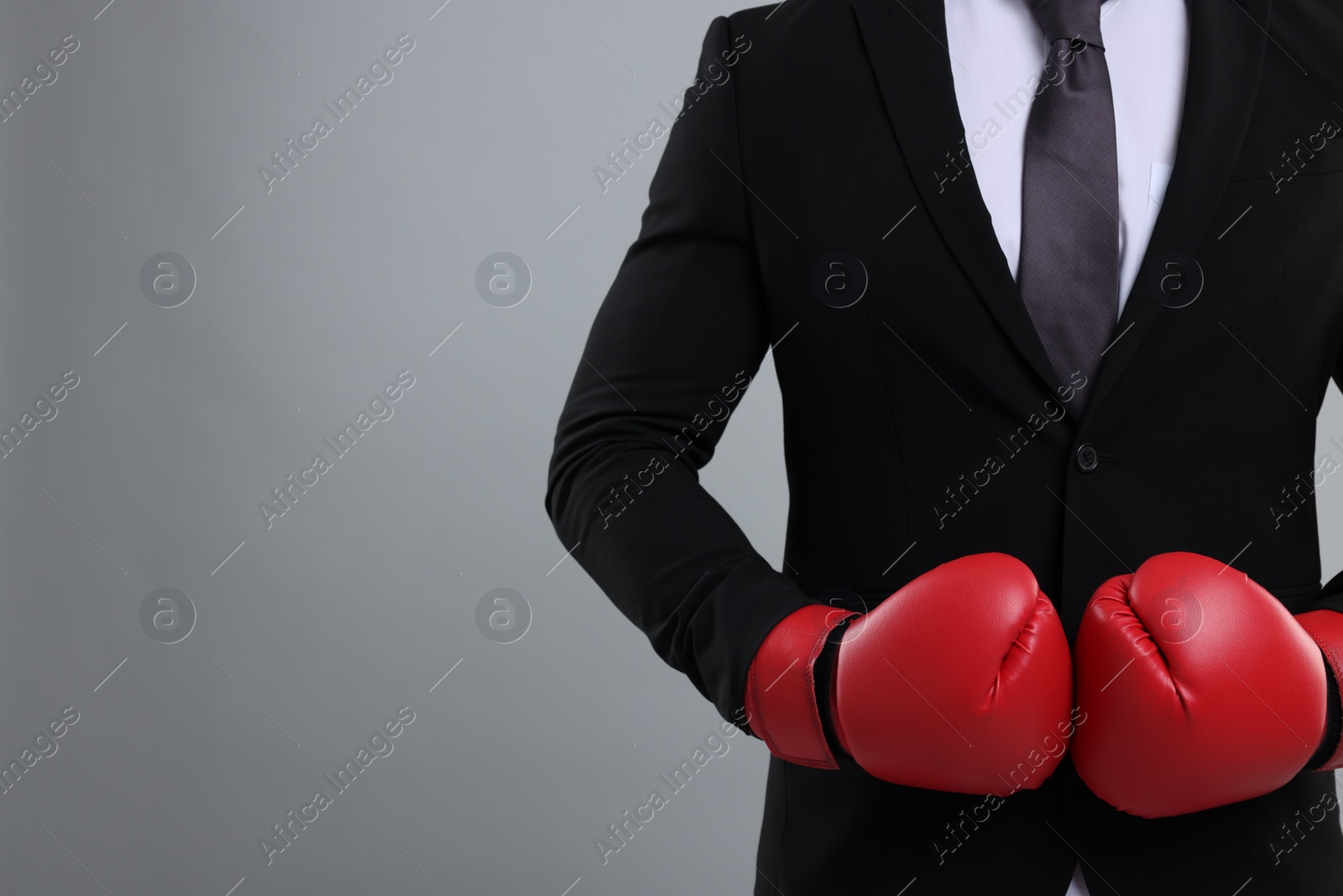 Photo of Businessman in suit wearing boxing gloves on grey background, closeup. Space for text