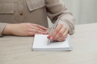 Woman writing in notebook at wooden table, closeup