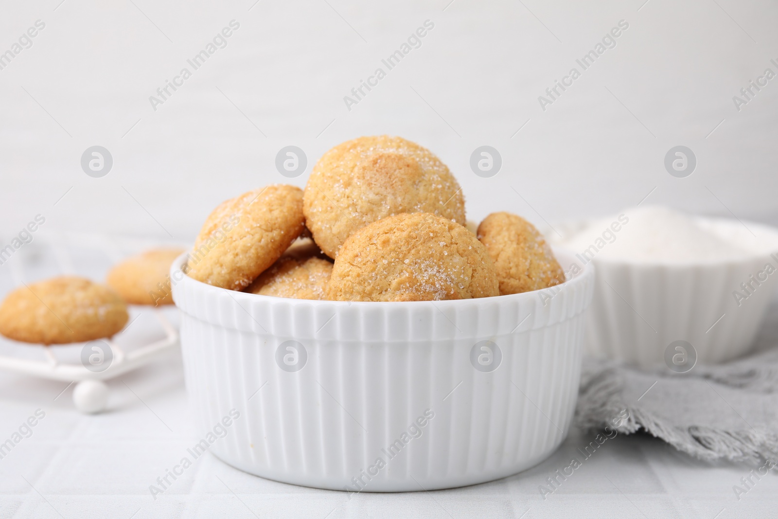 Photo of Tasty sugar cookies in bowl on white tiled table, closeup