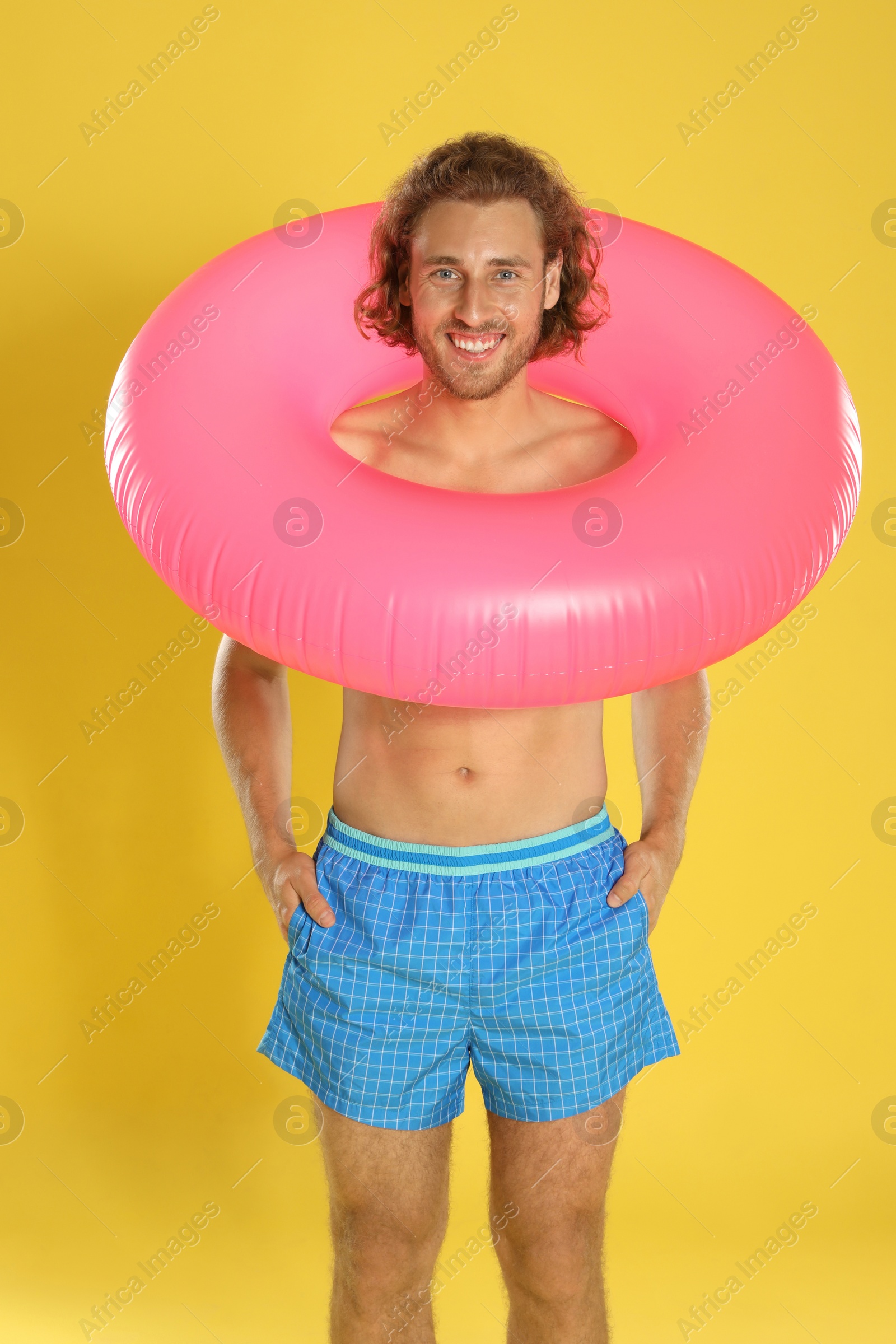 Photo of Attractive young man in beachwear with pink inflatable ring on yellow background