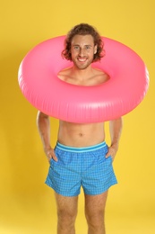 Attractive young man in beachwear with pink inflatable ring on yellow background