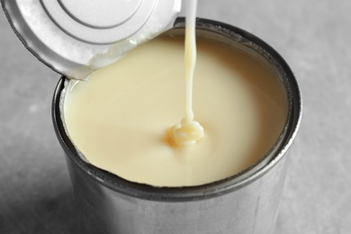 Photo of Condensed milk pouring into tin can on   grey background, closeup. Dairy product