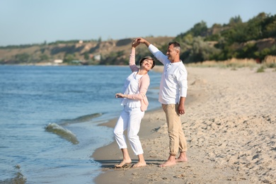 Happy mature couple dancing at beach on sunny day