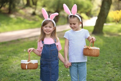 Photo of Easter celebration. Cute little girls with bunny ears holding wicker baskets outdoors