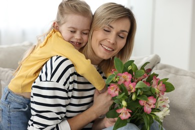 Little daughter congratulating her mom with Mother`s Day at home. Woman holding bouquet of alstroemeria flowers