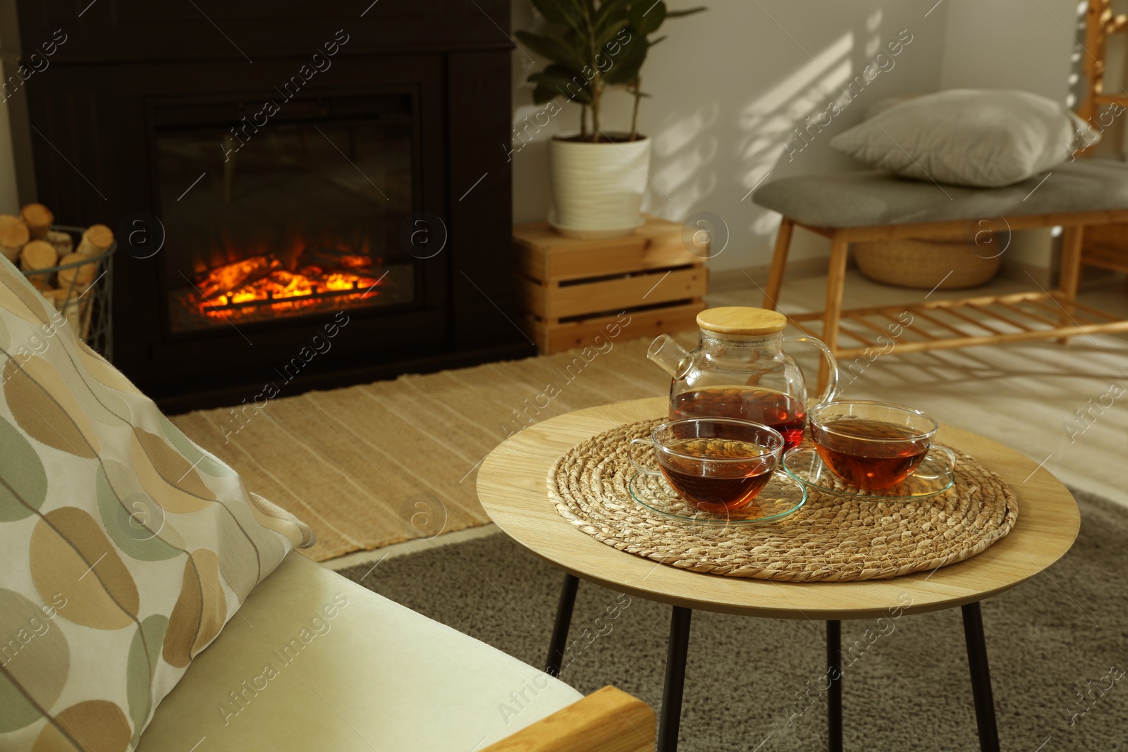 Photo of Teapot and cups of drink on coffee table near stylish fireplace in cosy living room. Interior design