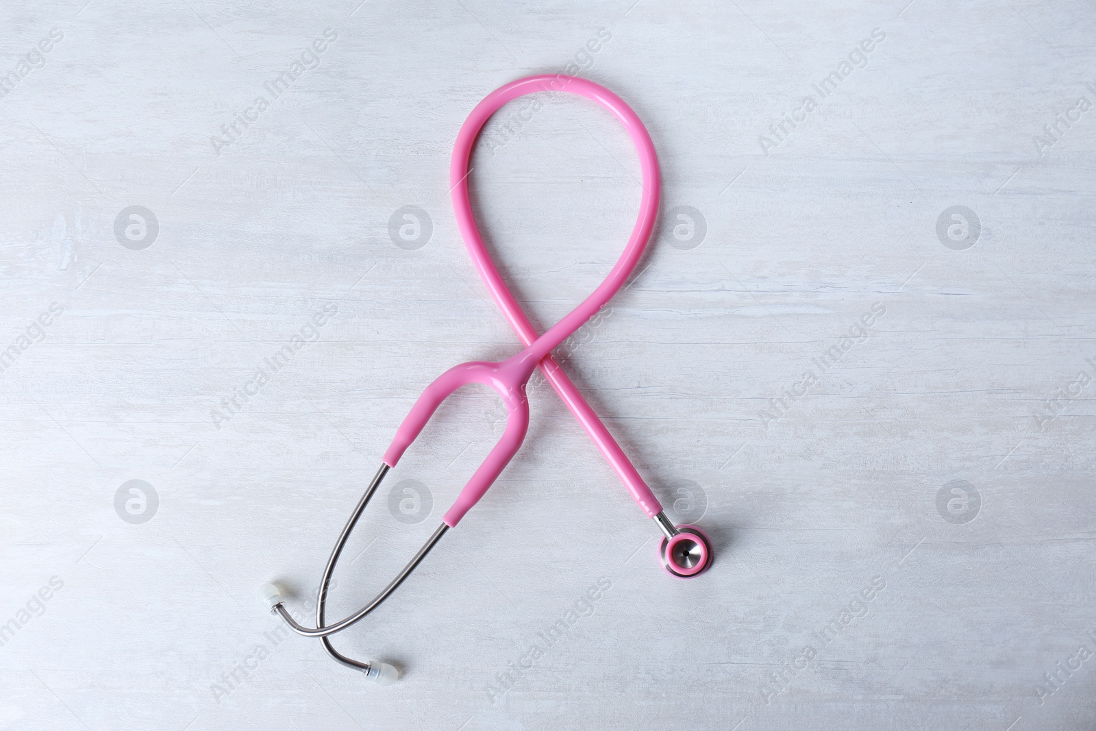 Photo of Pink stethoscope as awareness ribbon on light background, top view. Breast cancer concept