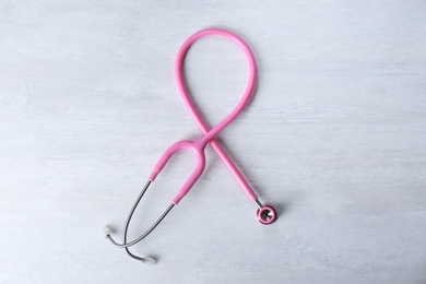 Photo of Pink stethoscope as awareness ribbon on light background, top view. Breast cancer concept