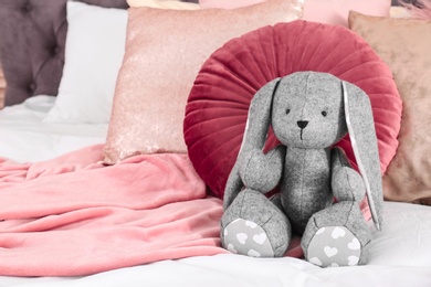 Photo of Cute toy rabbit on bed in child's room interior. Space for text