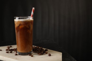Photo of Refreshing iced coffee with milk in glass and beans on table against dark gray background, space for text